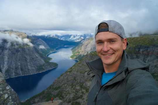 Young traveller taking selfie on the top with Beautiful fjord on background in Norway