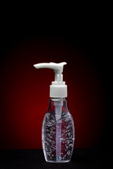 Small white and transparent hand dispenser with disinfection gel. Studio shot against a dark red background.