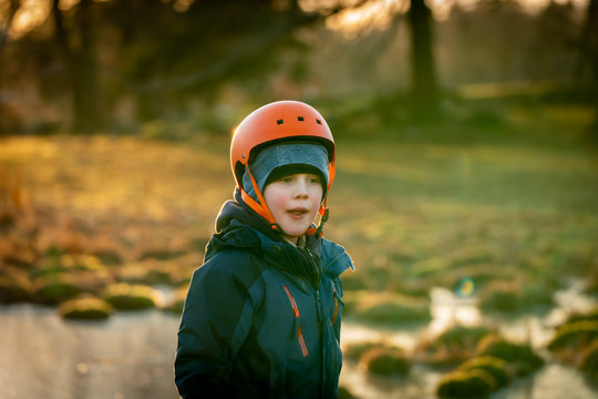 Young caucasian boy with winter clothing and helmet exploring frozen water at a green field. Winter sunset.