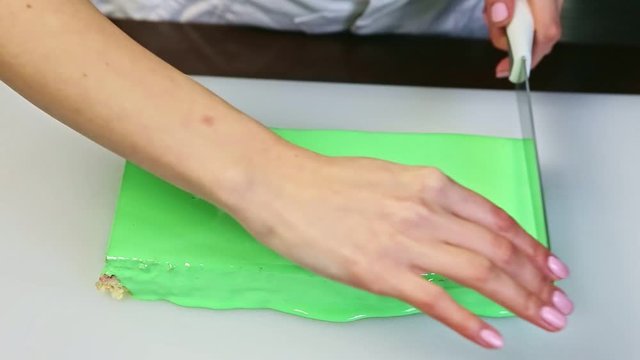 confectioner cut off by knife one edge of rectangle green glazed creamy layered cake