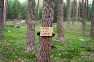 Teenage activist holding banner around a tree with environmental message. in the forest. Save our world. Concept of sustainability