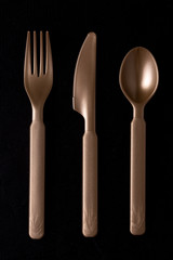 Fork, knife and spoon on a dark black surface shining a gold tint with reflecting highlights