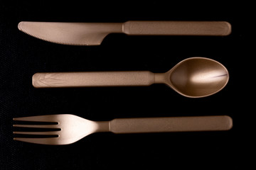 Close up of shiny dark gold coloured plastic cutlery set of horizontally ordered knife, spoon and fork laying face down