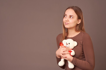 Fototapeta na wymiar Girl with a toy bear in her hands on a gray background. Gift for birthday, Valentine's day.
