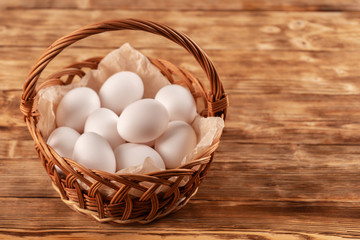 Farm eggs are laid on parchment in a wicker basket on a wooden table.
