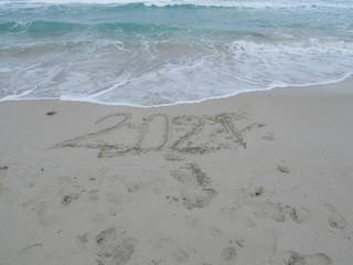 Happy New Year 2021, lettering on the beach with wave and clear blue sea. Numbers 2021 year on the sea shore, message handwritten in the golden sand on beautiful beach background. New Years concept.