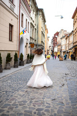 Obraz premium bride in a white dress walks down the street with a bouquet in her hand