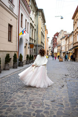 bride in a white dress walks down the street with a bouquet in her hand