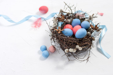 Painted Easter quail eggs in a nest of twigs with willow, feathers and ribbon on a white texture background with copy space. Top view