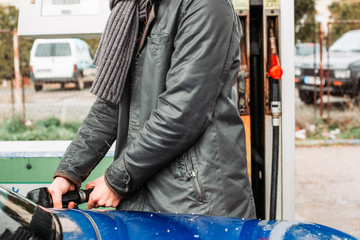 Fototapeta na wymiar Man hand holding fuel nozzle, refilling his car. Cold, rainy weather