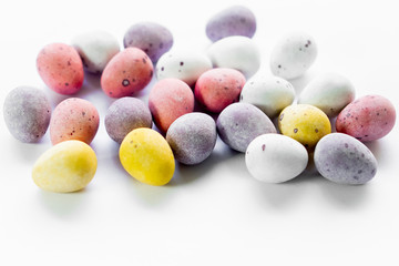 Sugar coated chocolate eggs, colorfull sweet easter treat. White background bright colours yellow, pink, violet and white eggs with dots. Copy text space, for wallpaper with easter theme.