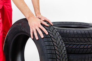 Obraz premium Zbliżenie mechanika rąk pchających czarną oponę w warsztacie.