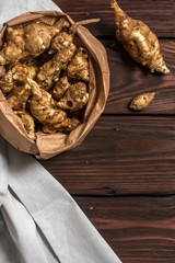 Several Jerusalem artichoke tubers in a paper bag on a wooden table with copy space. Helianthus tuberosus. Top view. Vertical orientation