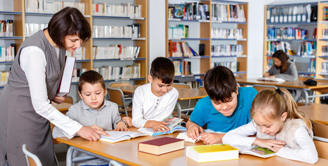 Group of school kids studying in school library with friendly female teacher