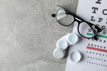 Glasses, case for contact lenses and eye test chart on grey background, top view