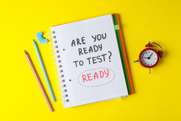 Inscription Are you ready to test? Ready, pencils and alarm clock on yellow background, top view