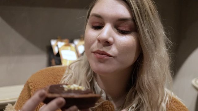 young Caucasian female model is  eating a delicious sweet chocolate brownie while enjoying the happy lifestyle of beauty and fashion. she looks around the cafe in bliss.