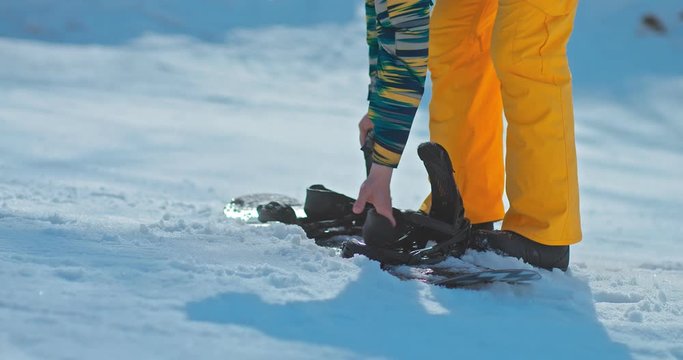 Snowboarder fastens the snowboard, fastens the board on his feet. Snowboarder puts his feet on a snowboard with buckles fastening. Close-up.