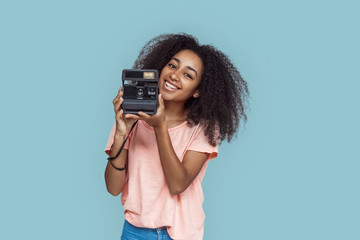 Freestyle. African girl standing isolated on gray with instant camera smiling happy