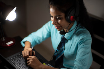 An Indian Bengali brunette young woman/telecaller in office wear is sitting on a office table in a working mood in a corporate office/bpo/call center. Indian corporate lifestyle