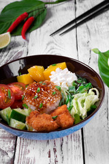 Poke bowl with fried chicken, vegetables and rice on the white wooden table. Hawaiian cuisine meal
