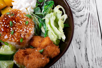 Poke bowl with fried chicken, vegetables and rice on the white wooden table. Hawaiian cuisine meal