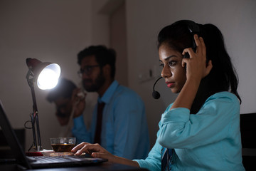 An Indian Bengali brunette young woman/telecaller in office wear is sitting on a office table in a working mood in a corporate office/bpo/call center. Indian corporate lifestyle
