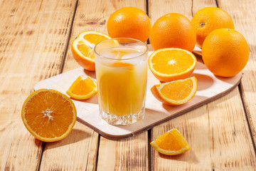 A glass of orange juice with ice cubes and a wooden board with oranges on a wooden table. Freshly squeezed orange juice.