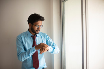 Fototapeta premium Portrait of an Indian Bengali tall, dark, handsome brunette young man in office wear is standing in front of a glass window in a corporate office/bpo/call center. Indian corporate lifestyle