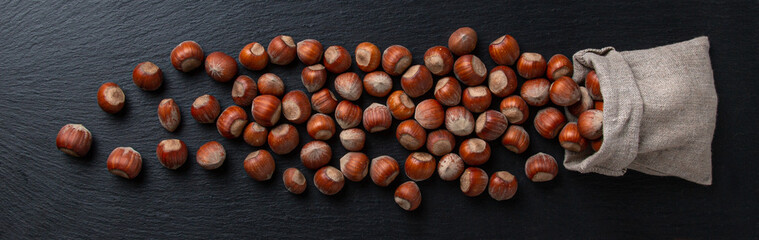 Obraz premium Hazelnuts in shells fall out of a linen bag on a black background with texture. Flat lay. 