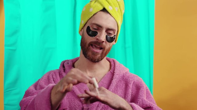 Portrait of bearded trans young man wearing pink bathrobe painting his hand nails singing alone smiling taking shower in the bathroom at home.