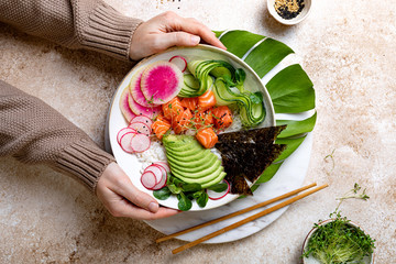 Girl holding Hawaiian salmon poke bowl with seaweed, avocado, watermelon radish and cucumber. Top...