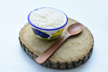Natural raw white rice grains, on display in bowl and wooden spoon