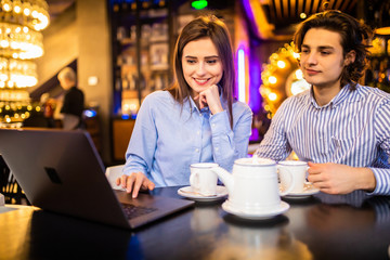 Beautiful young couple is using a laptop, talking and smiling while sitting in the cafe.