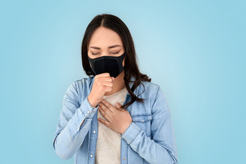 Coronavirus Concept. Chinese woman in respirator mask standing isolated on grey coughing concerned