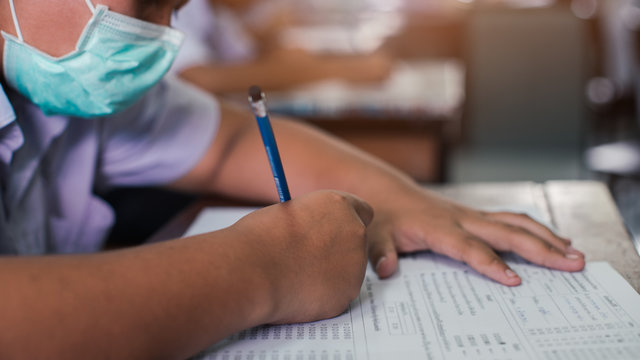 Students Wearing Mask For Protect Corona Virus Or Covid-19 And Doing Exam In Classroom With Stress.