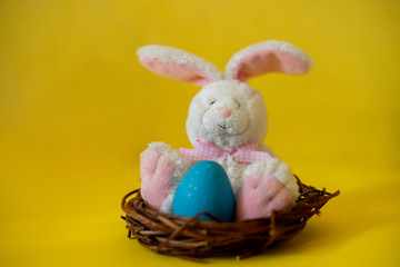 Easter bunny toy in nest with blue egg on yellow background. Easter concept.