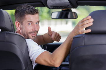 male driver turning to back of car with thumbs up