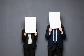 Business couple holding paper over their faces on gray background