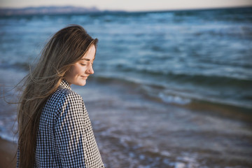 a pretty girl in a plaid dress and jacket walks along the sandy beach