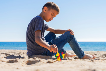 Autism awareness day concept. Boy teenager sitting on the beach with colorful puzzle autism awareness heart
