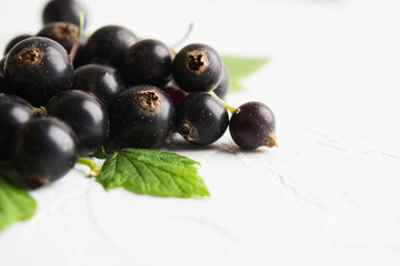 Stack of healthy fresh black currants with green leaves on white textured table