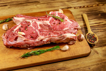 Raw fresh beef rib eye steak on bone with spices, garlic and rosemary on wooden table