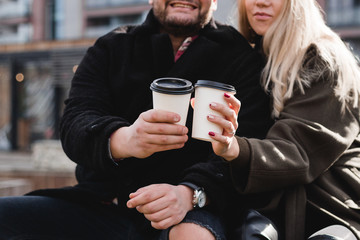 Young couple in love outdoor. Travelers with cups of coffee are walking in spring park. Beautiful sunny day. A young couple drinking coffee to go