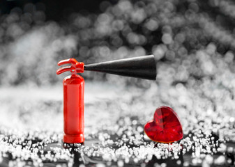 Miniature fire extinguisher standing next to a small red heart against a bokeh background