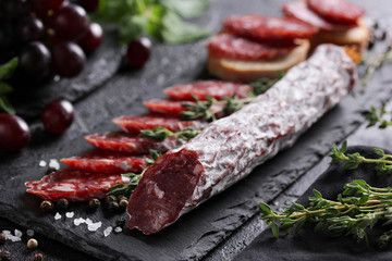 The concept of Italian cuisine. Sausage with truffle on a black board with grape, mint, thyme and spices. Background image, copy space