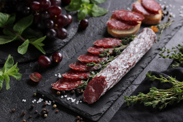 The concept of Italian cuisine. Sausage with truffle on a black board with grape, mint, thyme and spices. Background image, copy space