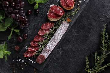 The concept of Italian cuisine. Sausage with truffle on a black board with grape, mint, thyme and spices. Background image, copy space
