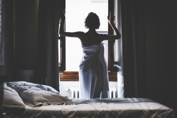 The charming girl had just woken up and went up to the window in the sheet. Back view. The concept...