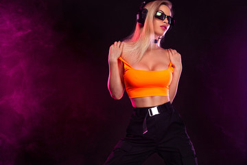 Sporty fit woman dancer and dj with headphones in sunglasses on dark background.